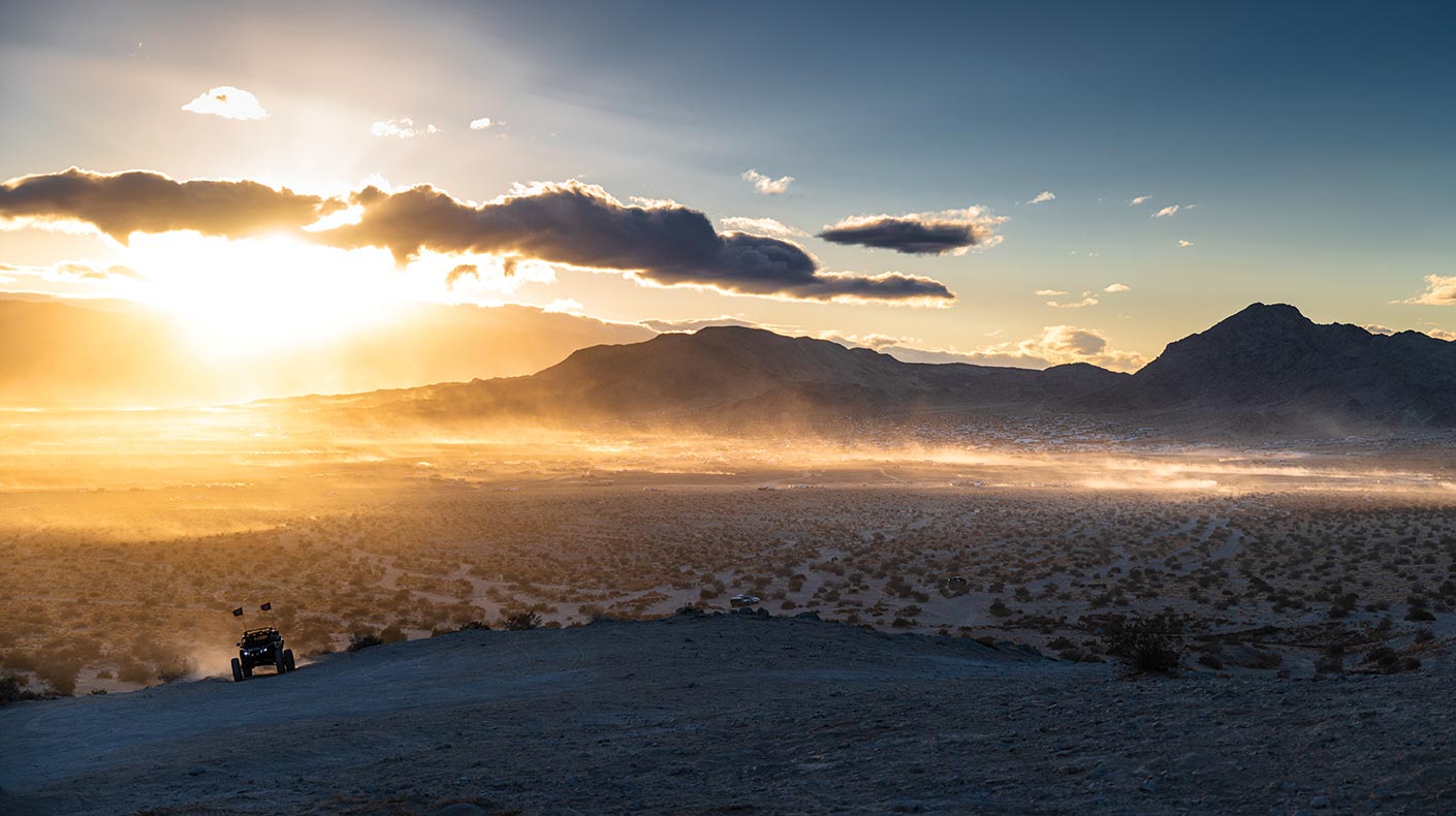 Lone off-road vehicle on a ridge in the desert with the sun setting in the background