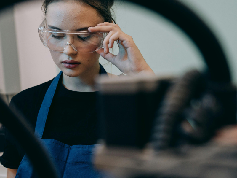 Woman with safety googles and apron on reading something.
