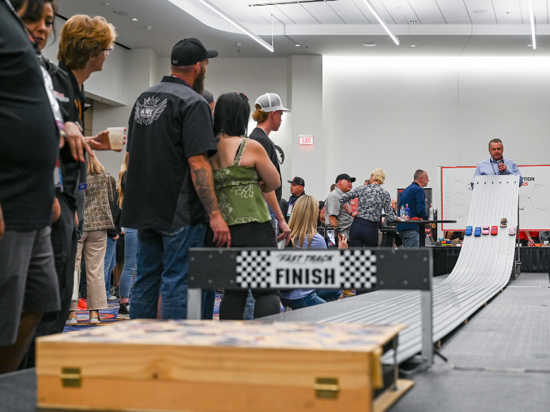 TORA Reception attendees look on as pinewood cars race on track.