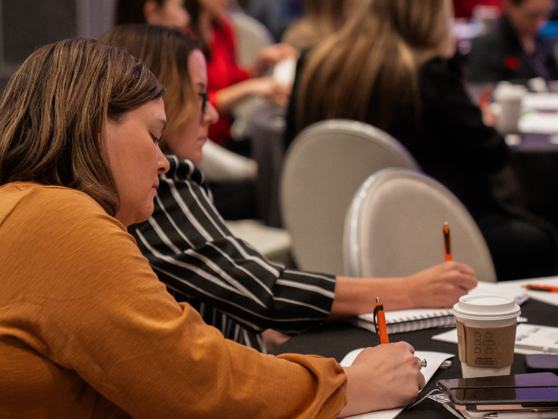 Two women taking notes at a Women's Leadership Forum session