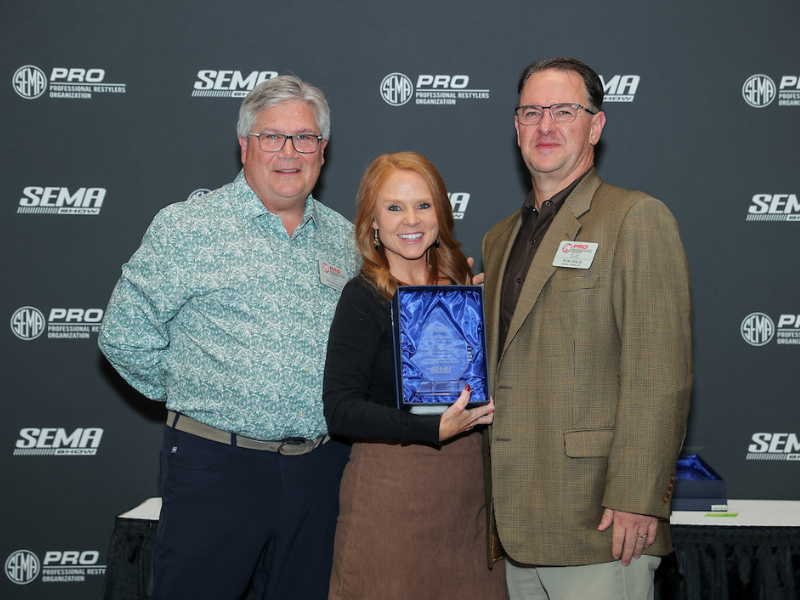 Two men and a woman posing with an award
