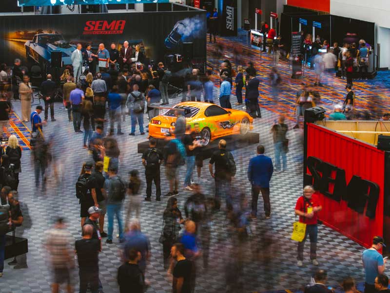 A crowded vehicle display and stage at the SEMA Show.