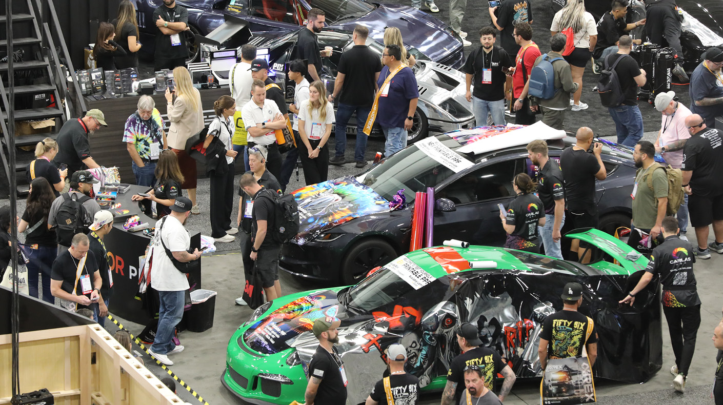 An image of a packed SEMA Show booth with three car displays.