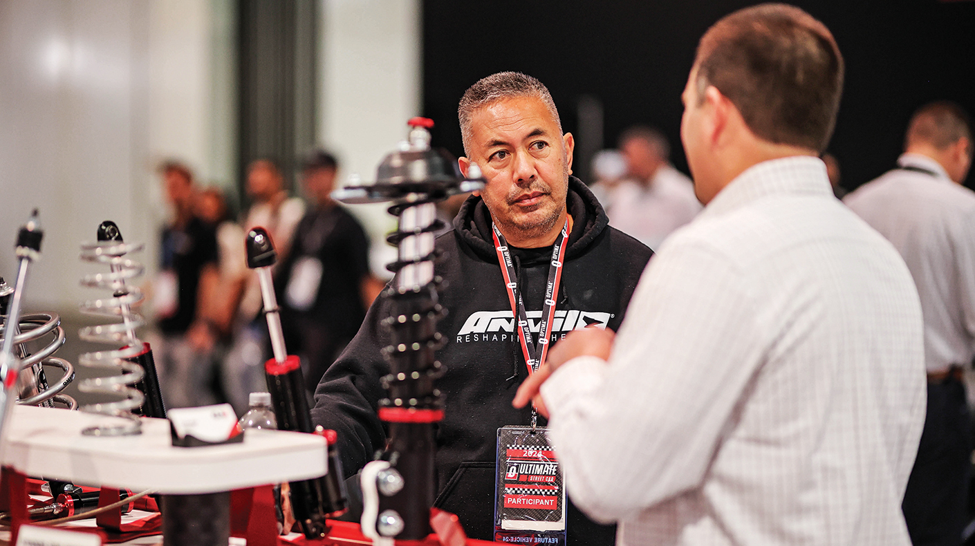 An exhibitor speaking with a SEMA Show attendee in a booth.
